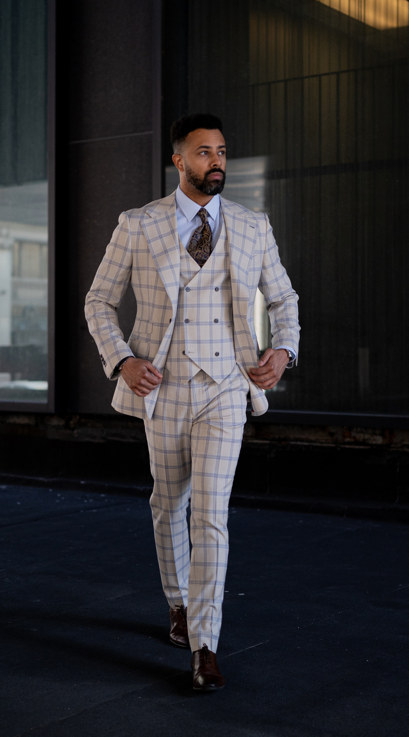Person wearing a beige and blue windowpane three-piece suit walking outdoors.