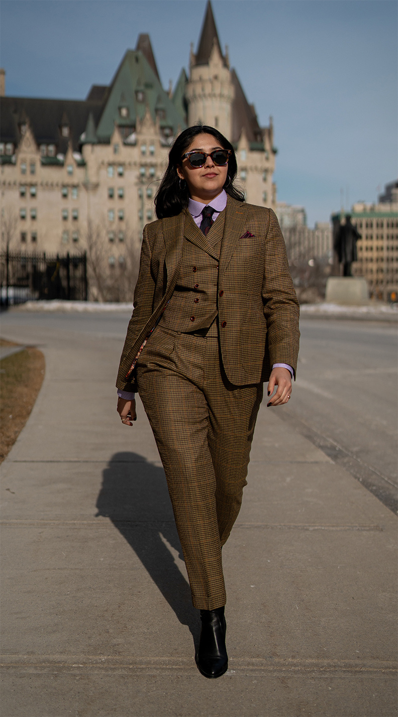 Woman wearing a brown plaid three-piece double-breasted suit walking confidently down a city sidewalk, showcasing a tailored women’s suit street style look.